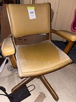 Front view of mustard vinyl swivel armchair showing wood frame, armrests and seat wear