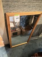 Full view of rectangular mirror with light wood frame leaning against wall