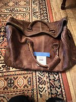 Overall view of Roots brown leather duffel showing handles, shoulder strap, zipper top, and front flap pocket