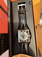 Front view of watch inside box showing skeleton dial and leather strap