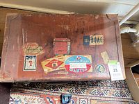 Top view showing brown leather surface with multiple vintage travel stickers and overall wear