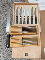 Group view: carving knife, six black-handled steak knives, twelve stainless steak knives in two wooden trays