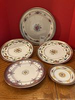 Five plates displayed upright and flat showing floral patterns and silver rims