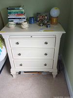 Front view showing three drawers, metal knobs, bracket feet, cream finish