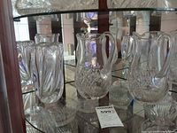 Pair of Tiffany pitchers and Orrefors vase on display shelf
