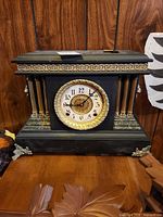 Front view of black mantel clock with brass columns, marble trim and missing glass
