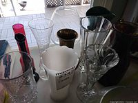 Group of assorted clear, colored and milk glass vases with brass piece on tabletop