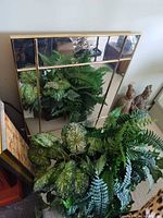 Mirror leaning against wall with artificial plant and warrior statues visible
