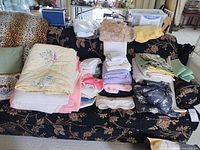 Sofa displaying pillows, folded towels, linens, quilt, fabric pieces and crochet items
