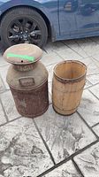 Metal milk churn and wood barrel side by side on pavement