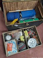 Steamer trunk open with lift-out tray showing sleeping bags, foam pad and assorted gear