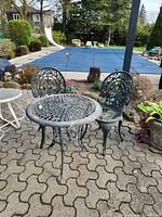 Outdoor cast metal bistro table with two matching chairs showing finish and wear