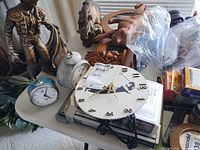 Overall lot showing two alarm clocks, paper-board clock face, carved wood figurine, additional decorative items