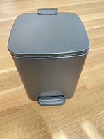 Front view of black matte plastic pedal trash can with closed lid and foot pedal visible