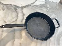 Top view of skillet showing interior surface, long handle, helper handle, pour spouts