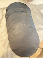 Stack of eight round black faux leather placemats on marble surface
