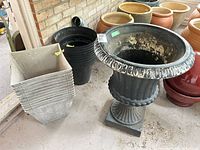 Overview of decorative urn, stack of square planters and black nursery pots