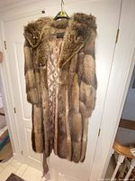 Front view of full-length brown fur coat on hanger, showing overall design and lining