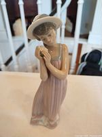 Front view of Lladró figurine showing girl holding flower, pastel dress and hat