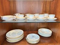 Upper shelf – eight Wedgwood teacups with eight saucers; left stack of small plates