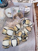 Bag of fabric-wrapped decorative balls and plastic container with metal napkin rings beside plates