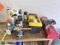 overview of workbench with toolboxes, wrenches, paint can, brush, jugs and aerosol cans
