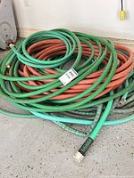Pile of coiled green and orange-red rubber garden hoses with metal connectors
