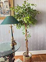 Lamp with green shade next to artificial tree in striped planter