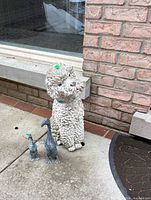 Concrete poodle statue and two metal duck statues beside brick wall