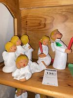Group of four Jullar ceramic angel figurines on wooden shelf showing various poses and size reference
