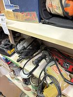 Shelf holding multiple corded power tools (drill, sanders, grinder) and charger showing wear and dust