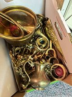 open box showing assorted brass items including bowl, pitcher, horn, candlestick parts, rings