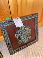 full view of plaque showing mask and wooden backing