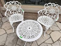 White cast aluminum round table with two matching ornate chairs on stone patio