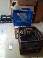 Stack of blue, beige, brown crates with stretch-wrap roll and basket visible