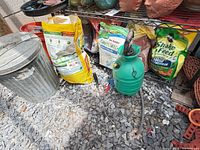 Overview of can, sprayer, grass seed and plant food bags on gravel floor