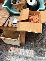 Overall view showing box of terra cotta pieces, metal hand tools, green tub, wicker basket, black planter