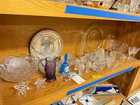 Shelf view with cut and colored glass items, bells, stemware, paperweights