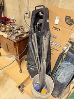 Black golf bag filled with multiple clubs next to bucket of loose clubs