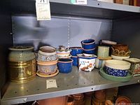 Shelf holding assorted ceramic and metal planters in various shapes and colours