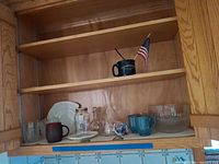 Cabinet shelf with mugs, glass carafe, Pyrex bowl, plates and additional glassware