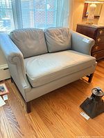 front view of light gray faux-leather settee showing cushions and wood legs