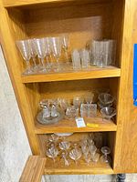Shelf with grouped etched glassware showing flutes, tumblers, coupes, cordial glasses, cruets, dishes and pitcher