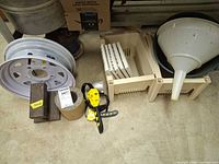 Group shot showing wheel rim, funnel, steel bar, lead cylinder, oil strap wrench, tiles in crate