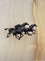 Front view of sterling brooch showing three galloping horses