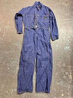 Full view of indigo denim coveralls laid flat showing overall design, sleeves, legs, and zipper closure