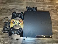 PS3 Slim console, three controllers, power cable, charging dock overview