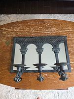 Front view of mirrored sconce showing three candle arms and ornate arches