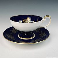 Side view of Aynsley cobalt blue teacup on saucer, showing gold floral design and gilt trim