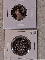 Both coins in individual flips, showing reverse designs (caribou quarter, Coat of Arms half dollar)
